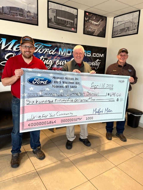 Community members holding a big check from Medford Motors for their annual Drive For Your Community charity event.