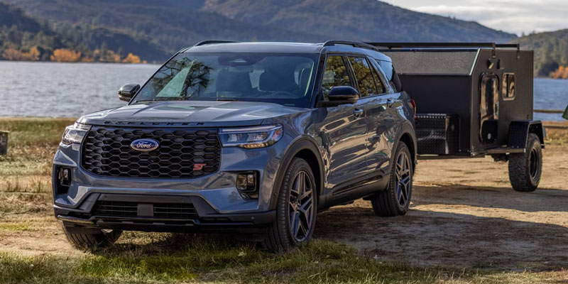 Gray 2026 Ford SUV parked near a lakeside in Medford, WI, towing a small trailer, with rugged styling, black wheels, and a scenic backdrop of water and forested hills.