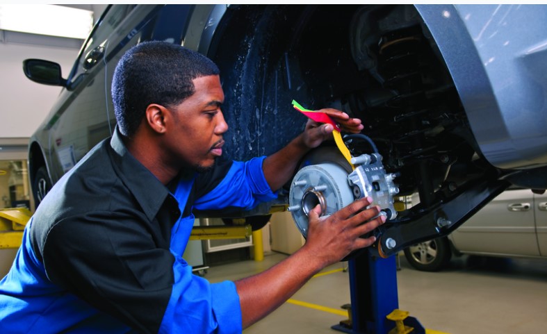 A mechanic working on the brake system of a vehicle, using tools to inspect and repair the components in an auto service shop.