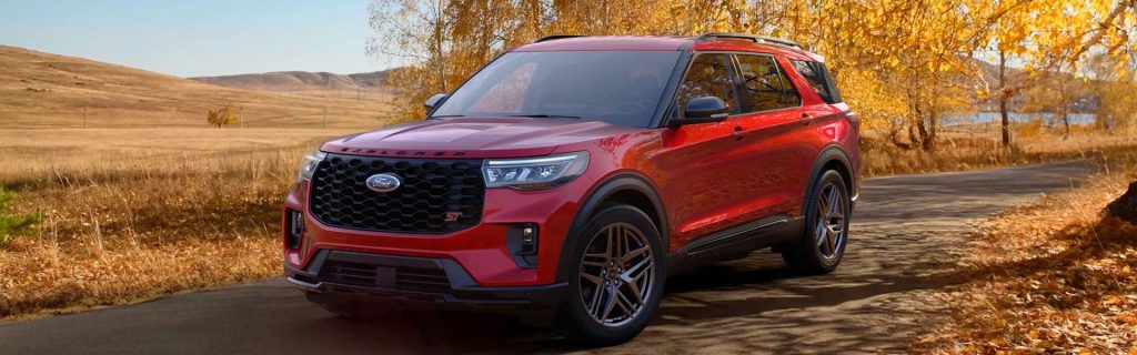 A red Ford Explorer parked on a scenic country road with autumn trees in the background.