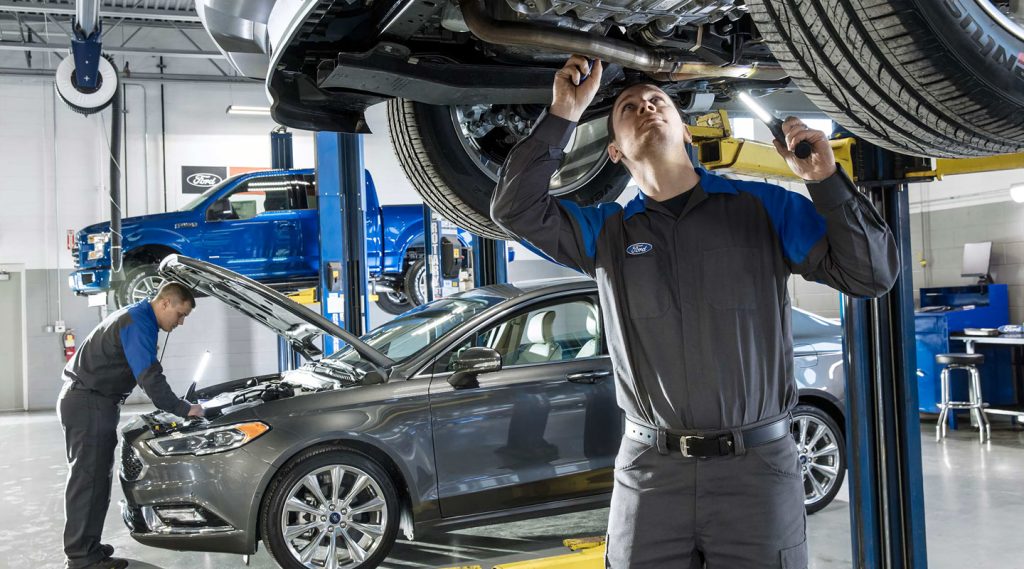 Two mechanics performing vehicle maintenance in an auto repair shop, with one working under a lifted car.